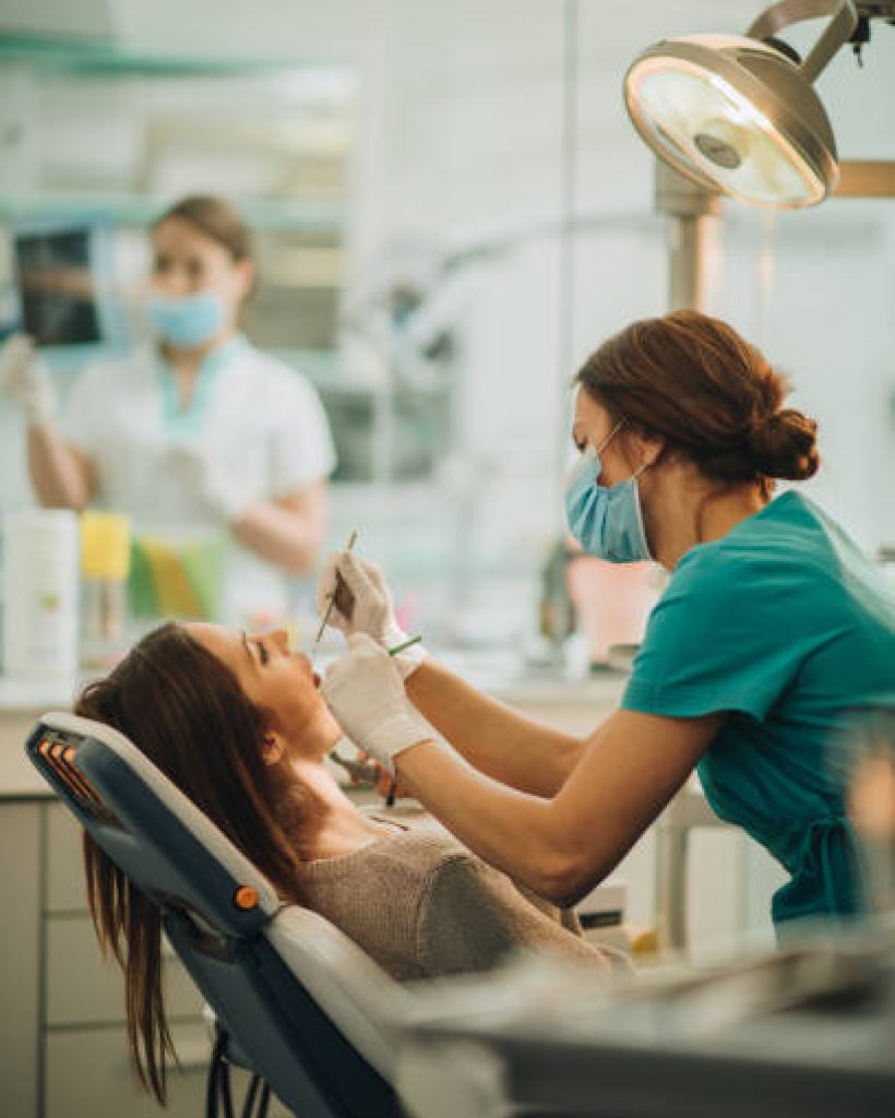 Female dentist examining young woman's teeth. There is person in the background.